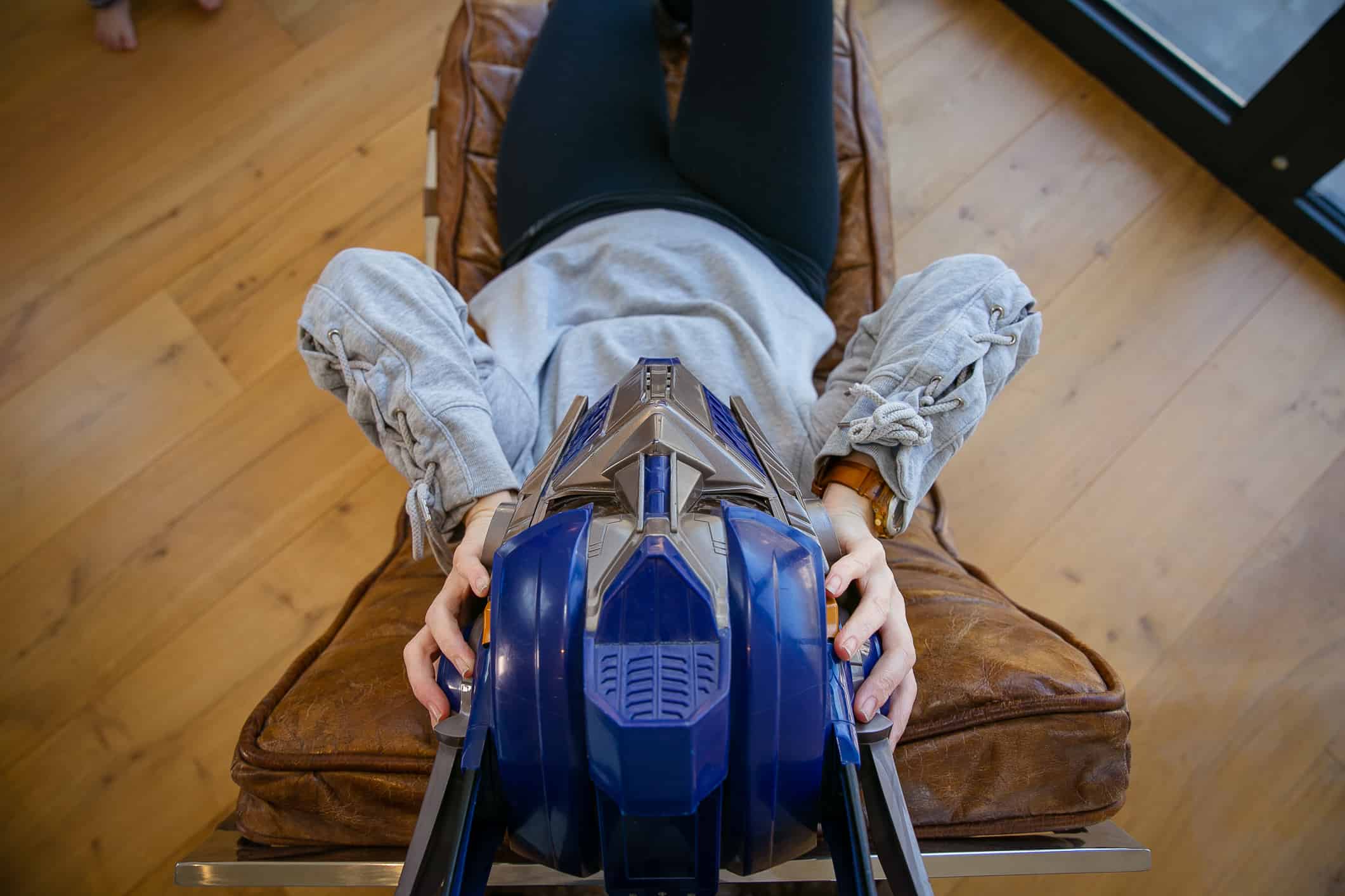 what-is-ptsd white woman in a brown leather chair wearing black jeans, grey jumper and a blue robot mask which represents the distressing symptoms caused by PTSD