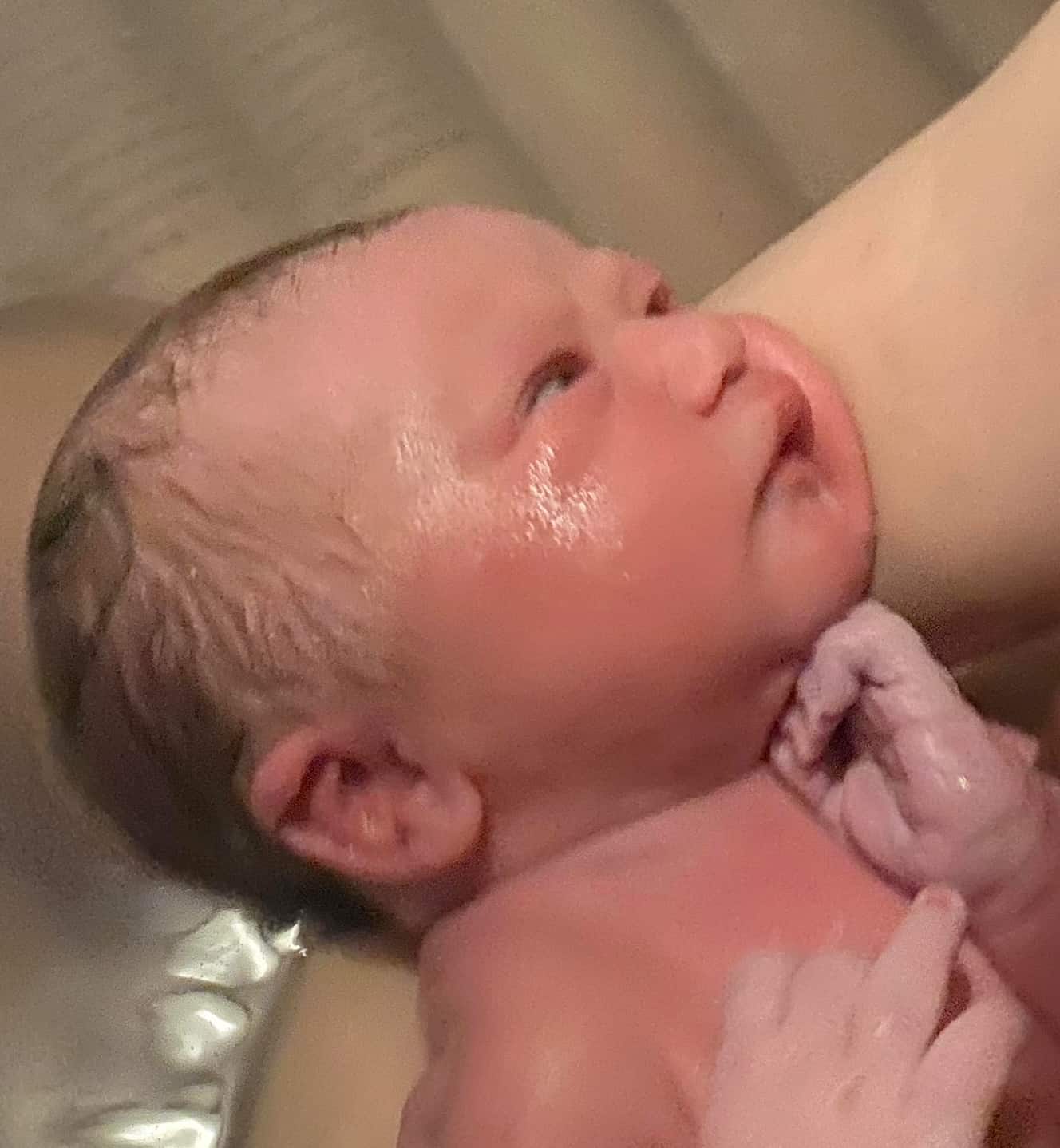 caucasian newborn baby just born in a birth pool at home and looking up at mother, mother out of camera shot only one arm visable