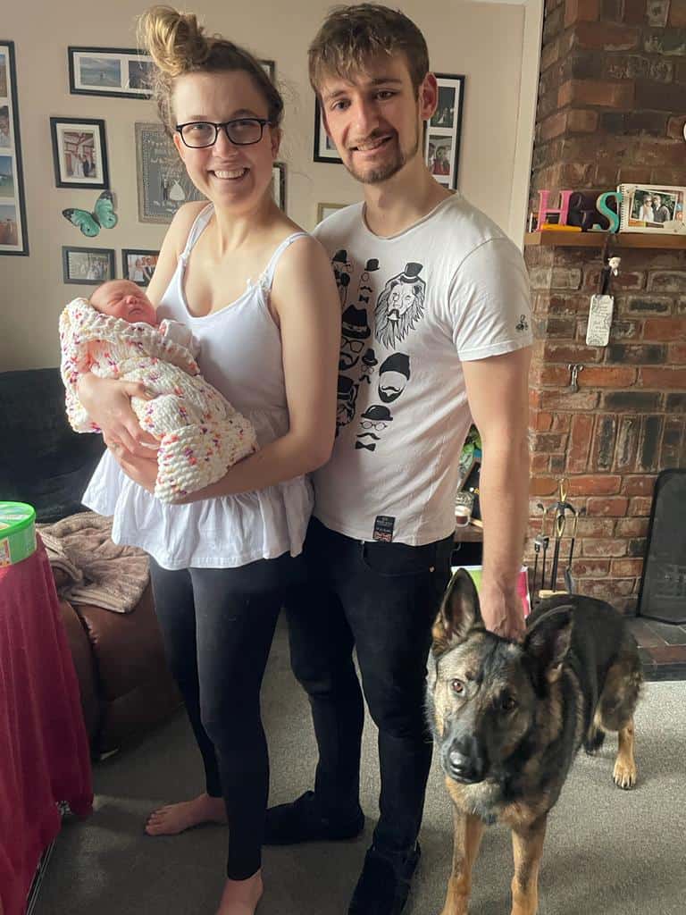 hannah and sean at home with their large pet dog beside sean and hannah holding their newborn daughter