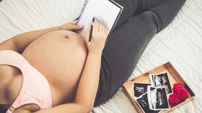 pregnant woman, face out of shot, relaxing on a bed with pen and paper as she makes notes on how to practice hypnobirthing and glove anaesthesia