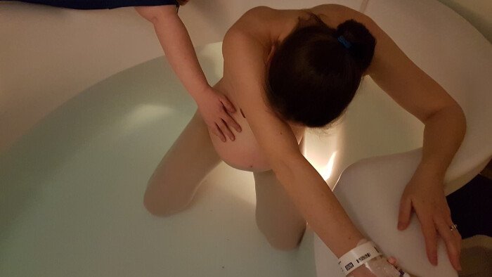 Water-birth-oxford-spires steph mcgee having a calm, natural, ivab in place, in a pool using the hypnobirthing technique of warm water for pain relief at the JR Oxford Spires Maternity Unit, a midwife out of shot but her arm can be seen palpating steph's bump