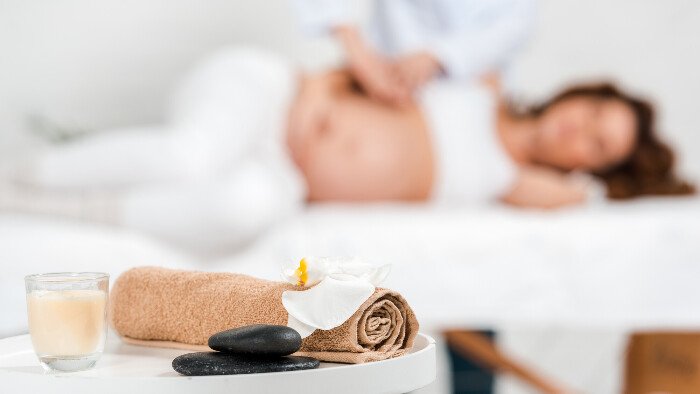 light-touch-massage-hypnobirthing calm birth setting with a candle burning and a white pregnant woman in the background lying on her side being massaged by a female birth partner who's using the light touch massage hypnobirthing technique for pain