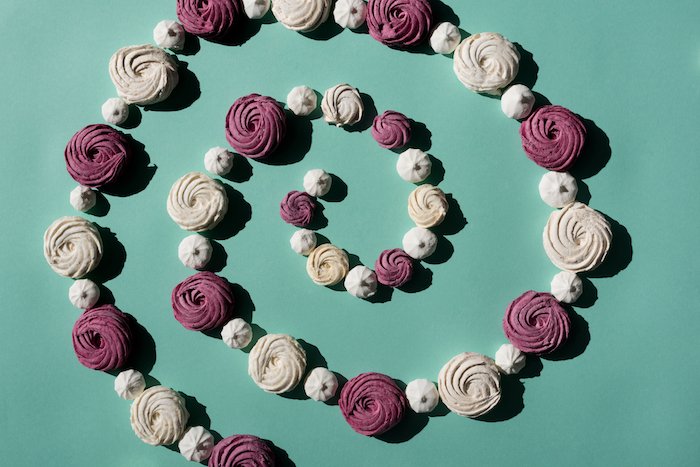 fertility-stress-hypnotherapy a spiral of mallow flowers in purple, white and cream against a teal background to demonstrate the spiral of infertility stress as well as the positive upward spiral of hypnotherapy that helps
