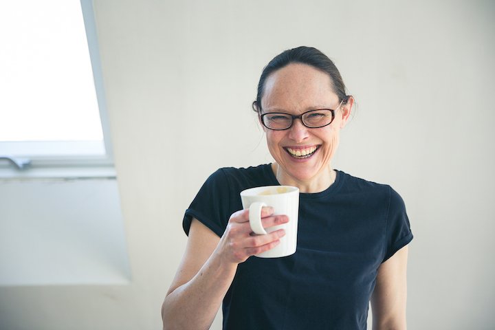 Steph McGee, Online Hypnotherapist in Oxford wearing a black t-shirt and drinking a frothy coffee after hypnotherapy for anxiety success with another client